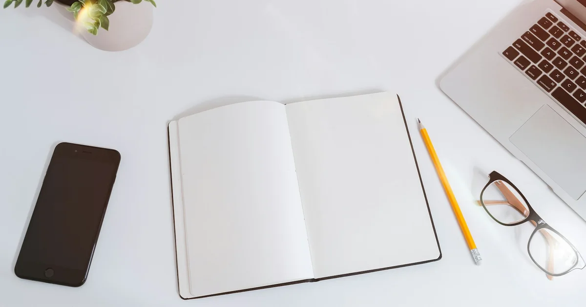 An open notebook beside a laptop on a bright desk