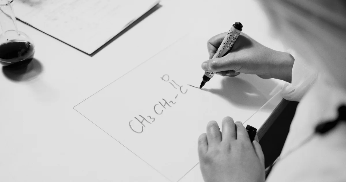 A hand drawing a chemical structural formula on paper